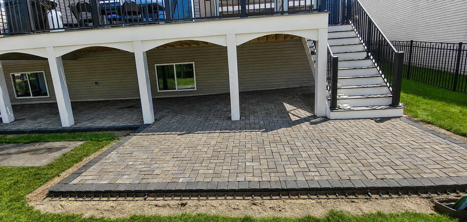 Raised paver patio with a stone seat wall and wood deck stairs