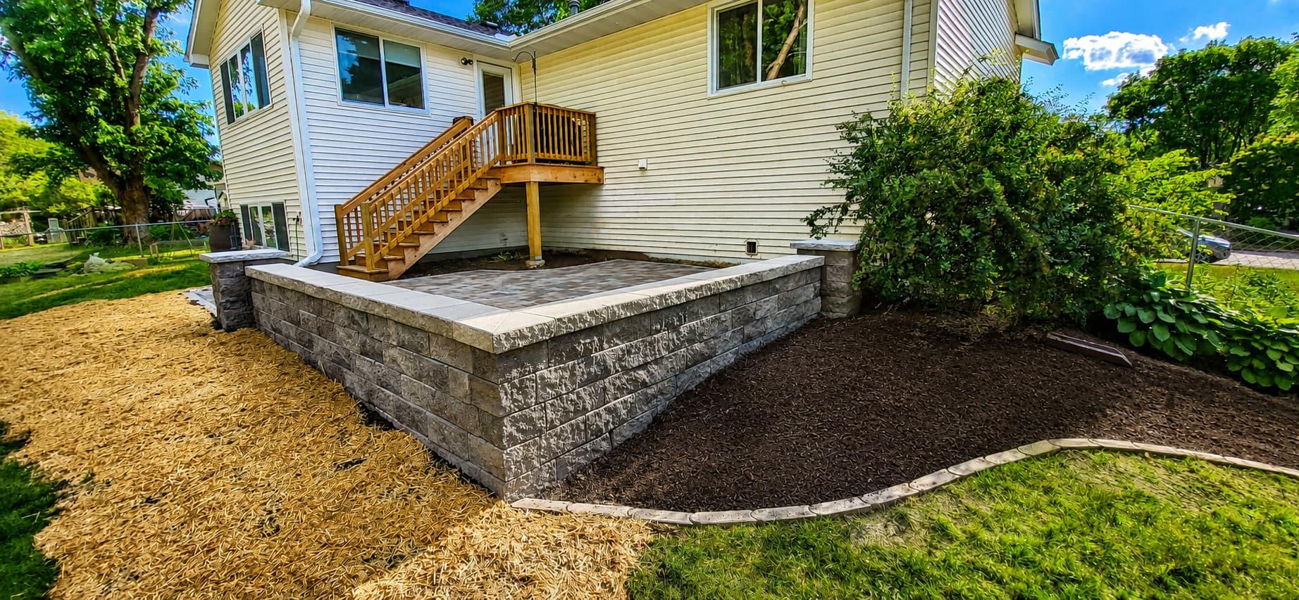 Stone retaining wall enclosing a raised patio with fresh mulch beds